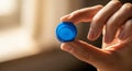 A hand is holding a small blue bottle cap between the thumb and index finger. The cap Royalty Free Stock Photo