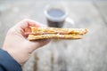 Hand holding a small cheese and ham sandwich in front of a cup of coffee Royalty Free Stock Photo