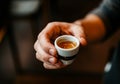 Hand holding small cup of fresh espresso in cozy cafe setting Royalty Free Stock Photo