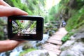 Hand holding small outdoor camera, filming photographing or taking pictures of tourists on wooden walk path in Prosiecka Valley