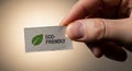 Hand holding a small rectangular label with the text ECO-FRIENDLY and a green leaf icon Royalty Free Stock Photo