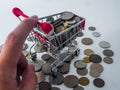 Hand holding small shopping cart with various currency coins using as shopping online or marketing concepts
