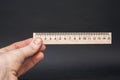 Hand holding small wooden ruler on a black background