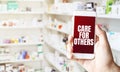 hand holding smart phone in pharmacy drugstore. Text CARE FOR OTHERs