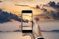 Hand holding smart phone taking photo of sunset landscape in vertical composition, in summer vacation time