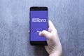 Hand holding smartfone with crypto currency logo Libra and buy button against gray blurred background.