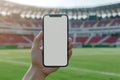 Hand holding smartphone with blank screen by the football stadium on the background. Generative AI Royalty Free Stock Photo