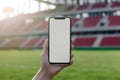 Hand holding smartphone with blank screen by the football stadium on the background. Generative AI Royalty Free Stock Photo