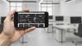 Hand holding smartphone with blueprint on screen in office Royalty Free Stock Photo