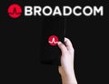 Hand holding smartphone with Broadcom logo on screen against dark background illustrative Royalty Free Stock Photo