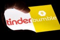 Hand holding a smartphone with a Bumble and Tinder dating apps icons on screen at night.