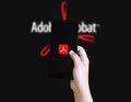 Hand holding smartphone displaying Adobe Acrobat app logo against blurred brand background illustrative Royalty Free Stock Photo