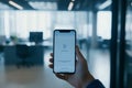Hand holding smartphone displaying application interface in modern office space, showcasing technology and connectivity with Royalty Free Stock Photo
