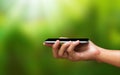 Hand holding a smartphone and an empty screen for your design on a natural green background in the morning concept. Mobile phone Royalty Free Stock Photo