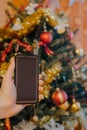 Smartphone in xmas. Hand showing a smartphone against Christmas tree at home