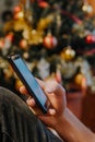 Smartphone in xmas. Hand showing a smartphone against Christmas tree at home