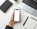 Hand holding smartphone over workspace with laptop and notebook Royalty Free Stock Photo