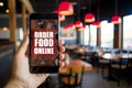 Hand holding smartphone showing ORDER FOOD ONLINE app in cozy restaurant ambiance