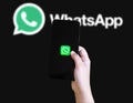 Hand holding smartphone with WhatsApp app icon on screen and logo in background illustrative editorial Royalty Free Stock Photo