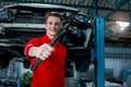 Hand holding spanner with blurred background of mechanic man in red uniform work with lifted vehicle, auto mechanic checking Royalty Free Stock Photo