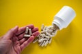 Hand holding spilled medical pills from pill bottle on yellow background Royalty Free Stock Photo