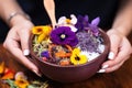 hand holding a spoon above an acai bowl garnished with edible flowers