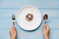 Hand holding spoon and fork above white dish with pink Measuring tape on blue pastel color wooden table. dieting , weight loss and Royalty Free Stock Photo