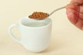 Hand holding a spoon with instant coffee over coffee cup