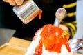 Hand holding a stainless cup pouring strawberry syrup on top of Bingsu Frozen cow`s milk make spinning to snow flake