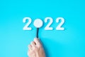 Hand holding Stethoscope with 2022 number on blue background. Happy New Year for healthcare, Insurance, Wellness and medical