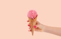 Hand holding strawberry ice cream cone on faded pastel color background.