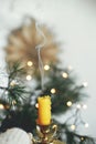 Hand holding stylish vintage candlestick with extinguish candle and smoke on background of warm lights, fir branches and sweden