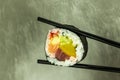 Hand holding sushi roll using chopsticks on gray background Royalty Free Stock Photo