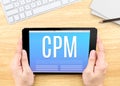 Hand holding tablet with CPM Cost per mille word on wood tabl