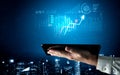 Hand holding tablet displaying data visualization and upward trend in statistics over a futuristic city skyline Royalty Free Stock Photo