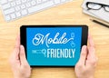 Hand holding tablet with Mobile friendly word on wood table , Dig Royalty Free Stock Photo