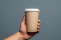 Hand holding takeaway paper coffee cup on a grey background