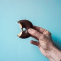 Hand holding a tasty bitten chocolate donut on the blue background