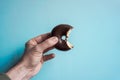 Hand holding a tasty bitten chocolate donut on the blue background