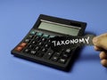 Hand Holding Taxonomy Sign over Digital Calculator on Blue Background for Financial Data Classification and Regulatory Reporting Royalty Free Stock Photo