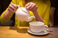 Hand holding a teapot pouring tea in a white cup