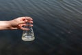 hand holding test tube for analyses with water on the background of the reservoir, the concept of water purity, pollution of water