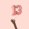 Hand holding a 13th birthday pink foil celebration balloon. 3D Rendering Royalty Free Stock Photo