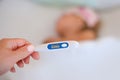 Hand holding thermometer foreground and sick little girl in bed