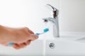 Hand holding toothbrush under flowing water from faucet