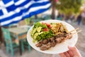 Hand holding a traditional greek pork souvlaki plate with fried potatoes and green salad. Royalty Free Stock Photo