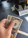 A hand holding two bills of one American dollar against the background of public transport. Selective focus Royalty Free Stock Photo