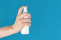 Hand holding up a white spray bottle, isolated against a blue background