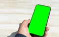 Hand holding upright black smartphone with chrome green screen on a light wooden table