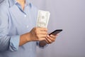 Hand holding of a US dollars banknote and using a smartphone while standing on gray background in the studio. Royalty Free Stock Photo